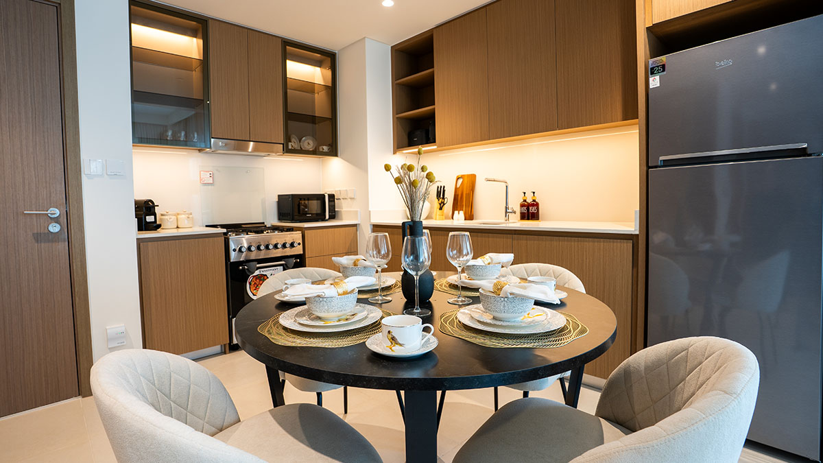 Modern apartment kitchen and dining area with wood cabinetry, integrated appliances and a set dining table ready for occupancy.