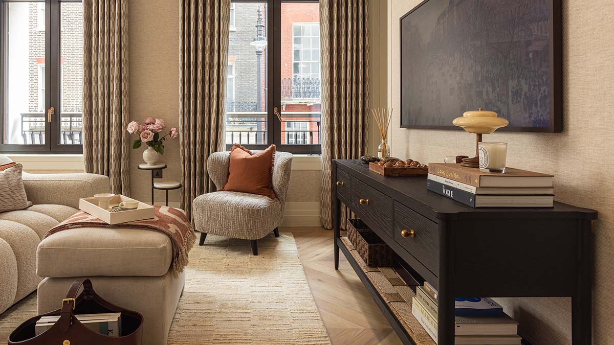 Elegant furnished living room with a cream sofa, rust accent cushions, dark wood console and floor-to-ceiling windows.